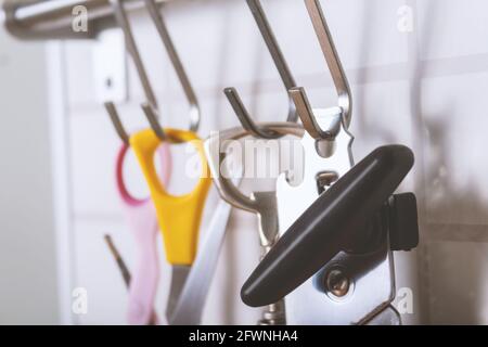 Cucina con gancio in acciaio inox su muro di mattoni bianchi. Foto ravvicinata del dispositivo di apertura delle lattine, delle forbici e del cavatappi. Profondità di campo poco profonda. Set di attrezzature da cucina. Foto Stock