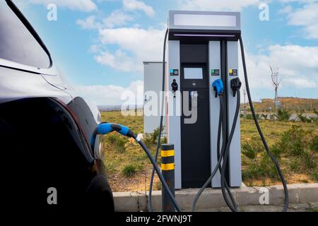 Auto EV collegata al caricabatteria e alla stazione di ricarica EV. Stazione di ricarica per auto elettrica vicino all'autostrada. Auto elettrica. Ricarica dell'auto a emissioni zero. Privo di carbonio Foto Stock