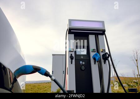 Auto EV collegata al caricabatteria e alla stazione di ricarica EV. Stazione di ricarica per auto elettrica vicino all'autostrada. Auto elettrica. Ricarica dell'auto a emissioni zero. Privo di carbonio Foto Stock