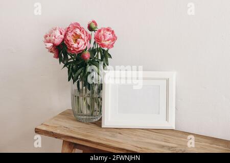 Scena floreale di natura morta. Fiori di peonie rosa, bouquet in vaso di vetro su tavolo di legno. Immagine bianca orizzontale mockup cornice. Matrimonio, compleanno Foto Stock