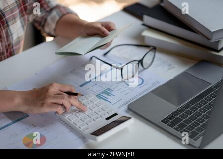 donna che controlla l'importo nel libretto del conto bancario con estratto conto bancario. Contabile che utilizza la calcolatrice per il settore finanziario Foto Stock