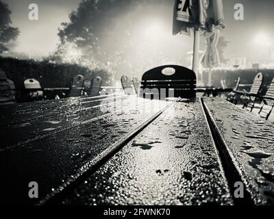 Drammatico scatto in scala di grigi di un tavolo da picnic in un parco vuoto dopo la pioggia Foto Stock