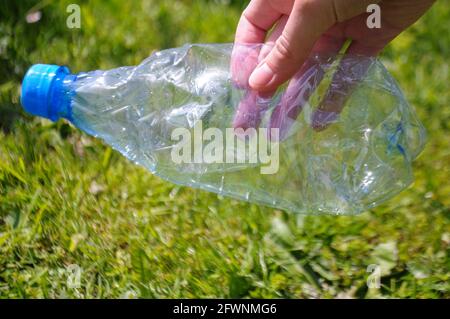 Primo piano su una mano che tiene una bottiglia d'acqua di plastica nel parco. Pulizia della messa a terra Foto Stock