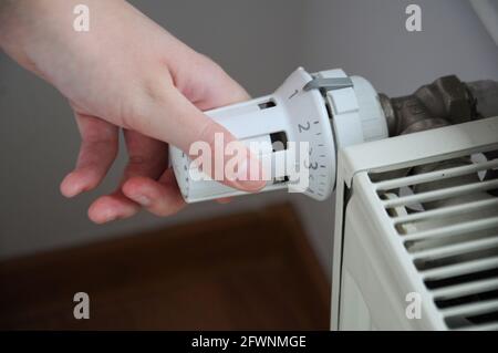 Primo piano su una persona che regola un termostato del radiatore bianco testa della valvola Foto Stock