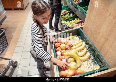 Una bambina sceglie le mele e le banane confezionate singolarmente nel negozio. Foto Stock