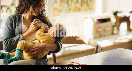 Madre che alimenta il suo neonato con il biberon a casa. Bambino bambino sdraiato sulla mano delle madri che beve il latte dal biberon. Foto Stock
