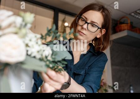 Ritratto di donna brunetta in bicchieri piegati su bouquet di fiori, lavoro fiorista messo a fuoco Foto Stock