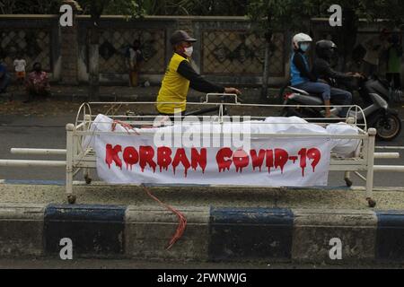 Madiun, Indonesia. 23 maggio 2021. I ciclisti e gli altri residenti hanno assistito all'azione teatrale della bara e dei corpi delle vittime del Covid-19 mentre si trovano nel mezzo della strada che collega le regioni. L'azione è un movimento di campagna per prevenire il virus corona o Covid-19 socializzando il protocollo sanitario 5M (Prokes), vale a dire lavarsi le mani con sapone con acqua corrente, indossare maschere, mantenere la distanza, limitare la mobilità e stare lontano dalla folla. (Foto di Ajun Ally/Pacific Press) Credit: Pacific Press Media Production Corp./Alamy Live News Foto Stock