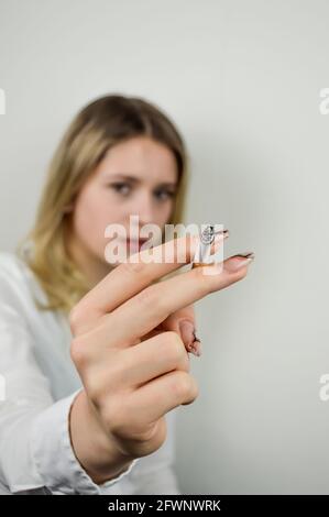 Ritratto di una bella giovane bionda che tiene una sigaretta davanti a lei, mettere a fuoco sulla mano e le dita Foto Stock