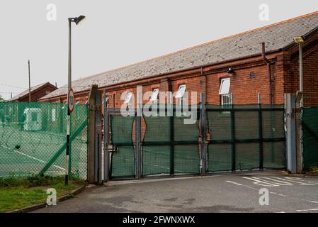 Dal settembre 2020, ex MOD Napier Barracks, Folkestone, sono state utilizzate dall'ufficio di casa per fornire alloggio temporaneo per i rifugiati maschi adulti che cercano asilo nel Regno Unito. Il campo è gestito da Clearspring Ready Homes. In precedenza, circa il 25% dei rifugiati nei campi ha dato risultati positivi per Covid-19, a causa di una grave mancanza di agevolazioni per le distanze sociali. Le caserme sono state dichiarate inadatte all'alloggio umano anche da ispettori indipendenti. L'alta recinzione intorno alle baracche di Napier è sormontata da filo spinato. Nella foto, ingresso alla caserma di Napier. Foto Stock