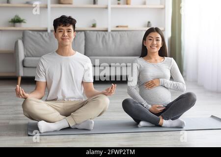 Positiva coppia asiatica incinta che fa yoga insieme Foto Stock