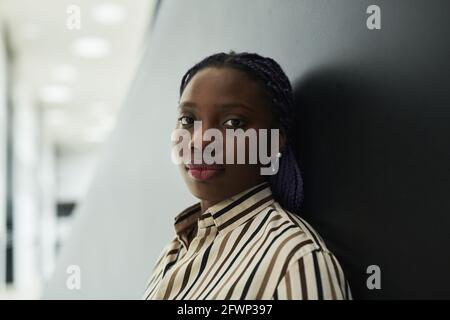 Primo piano ritratto di giovane donna d'affari afroamericana guardando la macchina fotografica mentre si è in piedi su sfondo nero in ufficio Foto Stock