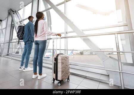 Percorsi di quarantena. Coppia nera in maschere mediche in attesa di volo in aeroporto Foto Stock