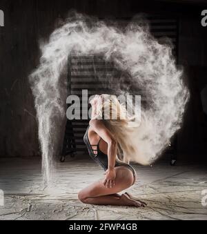 Bella danza bionda in nuvole di farina. La donna getta la farina nell'aria. Foto Stock