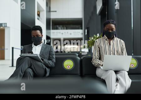 Ritratto grafico di due uomini d'affari che indossano maschere durante il lavoro in sala d'attesa all'aeroporto con divaricamento sociale Foto Stock