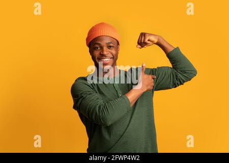 Allegro giovane uomo nero pompando pugno e indicando il suo Bicipiti Foto Stock
