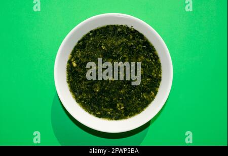 Famosa cucina araba tradizionale. Zuppa di molokhia in un recipiente bianco su sfondo verde. Disposizione piatta, vista dall'alto. Moroheiya, Mulukhiya Foto Stock