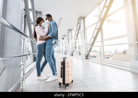 Viaggi pandemici. Giovane coppia nera in maschere mediche abbracciando in aeroporto Foto Stock