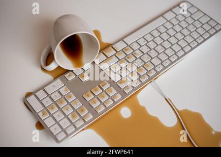 Caffè nero versato sulla tastiera di un computer a una luce bianca tabella Foto Stock