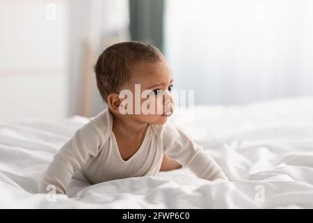 Carino piccolo afroamericano bambino strisciando sul letto a casa Foto Stock