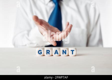 Mano di un uomo d'affari che presenta i cubetti di legno con la parola grant. Foto Stock