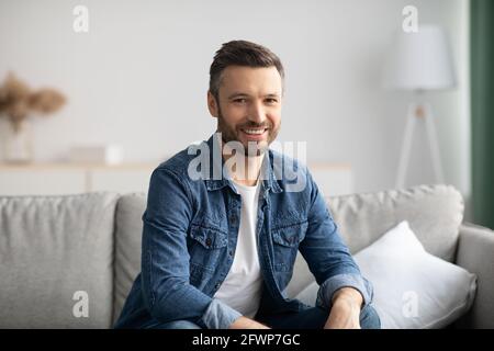 Felice uomo bearded che si rilassa sul divano a casa Foto Stock