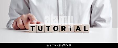 Uomo premendo il dito sui cubetti di legno con la parola tutorial. Foto Stock