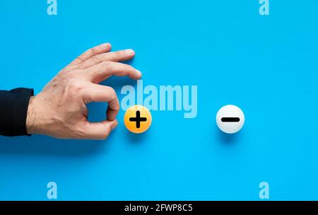 La positività supererà la negatività o i pro scarteranno il concetto di cons. La mano maschile sta per lanciare la palla con il segno più e sparare il meno. Foto Stock