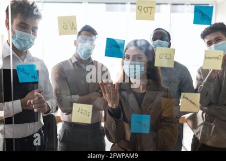 Uomini d'affari che hanno una riunione usando note post-it appiccicose sulla parete di vetro Foto Stock