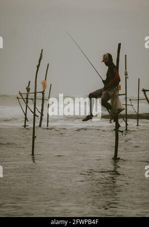 Pescatori tradizionali di swilt che tengono una canna da pesca e una borsa per raccogliere il pesce, seduti su una croce bastone sopra la superficie di acqua di mare pazientemente waitin Foto Stock