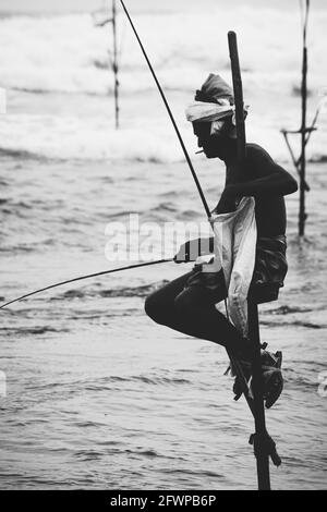 Mirissa, Sri Lanka - 07 26 2020: Silhouette di pescatori tradizionali, canna da pesca, e una borsa per la raccolta del pesce, seduto su una croce bastone sopra la Foto Stock