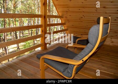 Vista su una foresta dal balcone di un moderno chalet in legno con due poltrone. Turismo e vacanza estiva concetto. Casa estiva in legno in una pineta Foto Stock