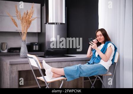 Donna e annoiati sbadigli guardare i media in un telefono cellulare seduti su un lettino a casa Foto Stock