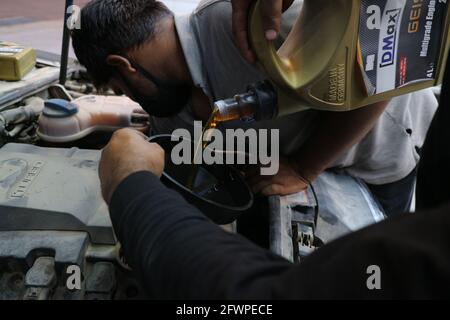 Kuwait City – Kuwait – 15 aprile 2021: Meccanico che lavora sulla macchina mentre un altro versa olio motore Foto Stock