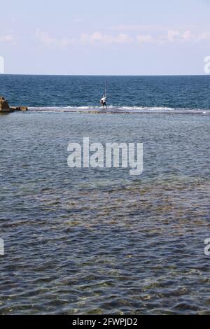 pescatore in piedi nell'acqua poco profonda per lanciare la canna da pesca Foto Stock