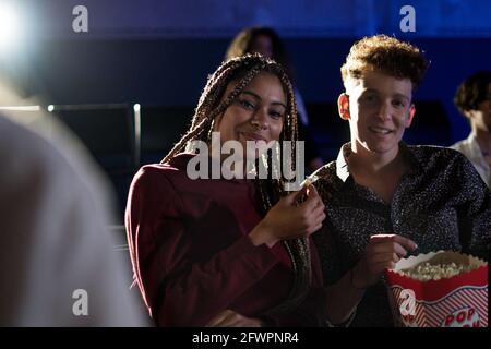 Giovane coppia che mangia popcorn mentre guardi un film al cinema, guardando la macchina fotografica. Foto Stock