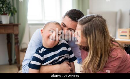 Ragazzo allegro sindrome giù con i genitori all'interno a casa abbracciando. Foto Stock