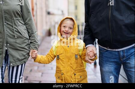 Bambino sindrome di Down con genitori irriconoscibili all'aperto in una passeggiata sotto la pioggia, tenendo le mani. Foto Stock