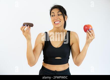 Giovane donna ispanica che tiene mela e ciambelle sorridendo con un sorriso felice e fresco sul viso. Mostrando i denti. Foto Stock