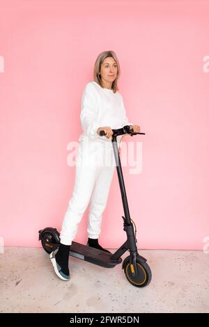 Una donna su Elettricità spingere Scooter su sfondo rosa, Studio Shot Foto Stock