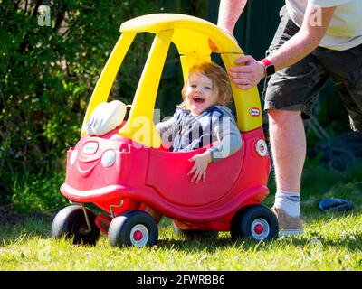 Papà che spinge il bambino in auto giocattolo Little Tikes, Regno Unito Foto Stock