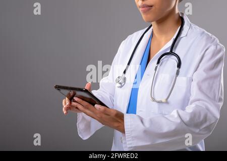 Metà della sezione della dottoressa afroamericana che usa una tavoletta digitale su sfondo grigio Foto Stock