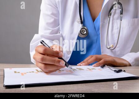 Sezione centrale del medico femminile che scrive sugli appunti contro il grigio sfondo Foto Stock