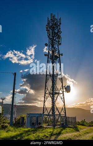 Silhouette di una grande antenna di comunicazione con nuvole illuminate da un tramonto arancione. Abruzzo, Italia, Europa Foto Stock