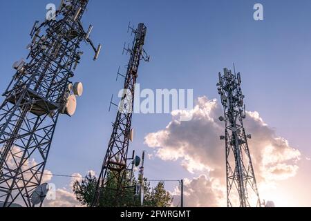 Tre antenne di comunicazione satellitari, cellulari o televisive si distinguono nel cielo con una nuvola illuminata dal sole che tramonta. Abruzzo, Italia, Europa Foto Stock