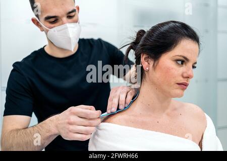 Fisioterapista maschile che dà massaggio al collo a una donna rilassata seduta in barella. Sta usando il nastro di kinesio. Foto Stock