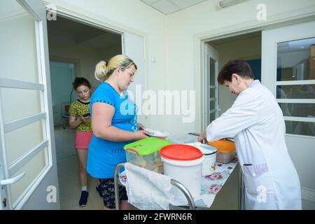 In una hall di un ospedale. Infermiere in camici da laboratorio che forniscono ai pazienti piatti con cibo da un carrello per vassoi. 4 giugno 2019. Kiev Centro cittadino di neurochirurgia. Foto Stock