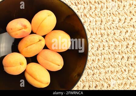 Diverse albicocche di ananas gialle mature in un piatto nero, primo piano, su un tappetino di paglia, vista dall'alto. Foto Stock