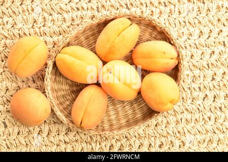 Diverse albicocche di ananas gialle in un piatto di paglia, macro, su un tappetino di paglia, vista dall'alto. Foto Stock