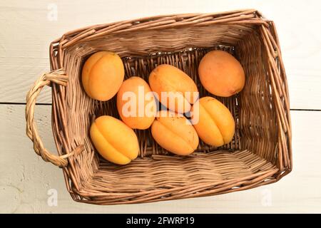 Diverse albicocche di ananas gialle mature in un cesto di ramoscelli, primo piano, su un tavolo di legno bianco, vista dall'alto. Foto Stock